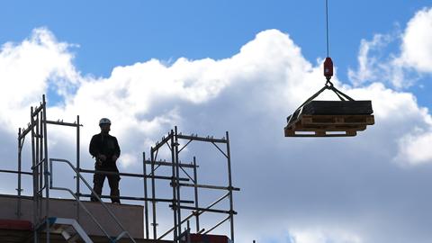 Bauarbeiter beobachtet auf einer Baustelle den Transport einer Palette durch einen Kran (dpa)