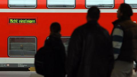 Fahrgäste auf einem Bahnsteig und ein Schriftzug „Nicht einsteigen“ leuchtet auf einem Regionalzug der Deutschen Bahn.