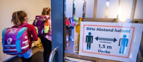 Schüler betreten eine Schule mit Hinweisschild auf die Corona-Regeln an der Tür. (dpa)