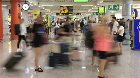 Reisende gehen am Flughafen von Mallorca durch eine Halle.