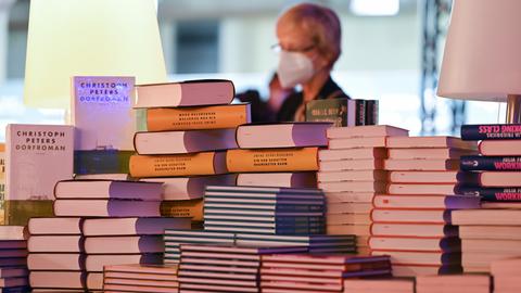 Eine Frau steht am Rande der Eröffnungspressekonferenz der Buchmesse in der Festhalle vor einem Stapel Bücher.  (dpa)