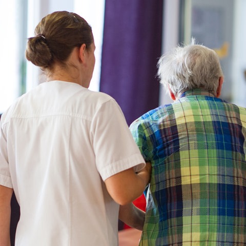 Zwei Pflegerinnen stützen einen Bewohner in einem Pflegeheim.