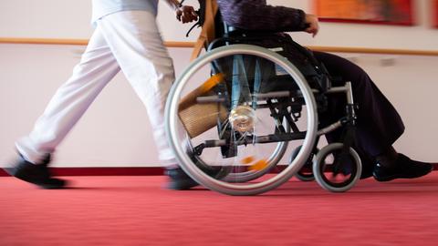 Ein Pfleger eines Pflegeheims schiebt eine Bewohnerin mit einem Rollstuhl. (dpa)