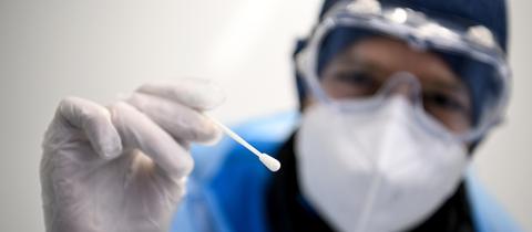 Ein Arzt in Schutzanzug hält ein Teststäbchen für die Entnahme einer Probe für einen PCR-Test in der Hand. (dpa)