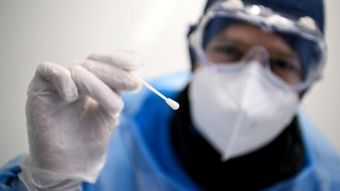 Ein Arzt in Schutzanzug hält ein Teststäbchen für die Entnahme einer Probe für einen PCR-Test in der Hand. (dpa)