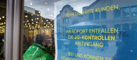 Ein Schild mit der Aufschrift "Ab sofort entfallen die 2G-Kontrollen am Eingang" steht am Zugang zu einem Kaufhaus in der Darmstädter Innenstadt.  (dpa)