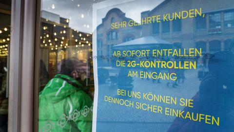 Ein Schild mit der Aufschrift "Ab sofort entfallen die 2G-Kontrollen am Eingang" steht am Zugang zu einem Kaufhaus in der Darmstädter Innenstadt.  (dpa)