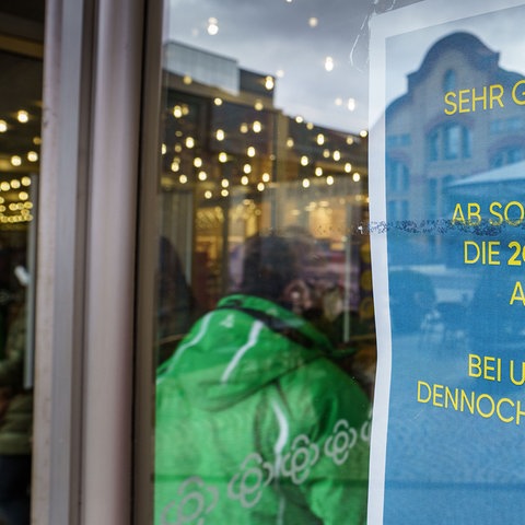 Ein Schild mit der Aufschrift "Ab sofort entfallen die 2G-Kontrollen am Eingang" steht am Zugang zu einem Kaufhaus in der Darmstädter Innenstadt.  (dpa)