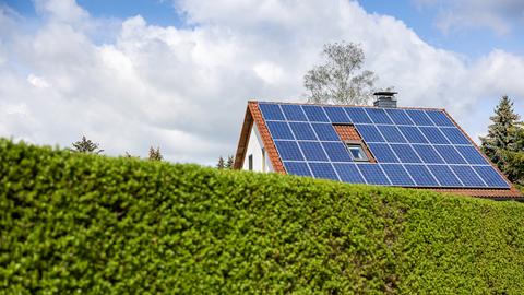Ein Einfamilienhaus mit Solarzellen auf dem Hausdach steht hinter einer Hecke. (dpa)