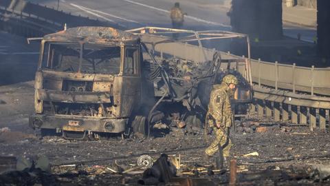 Ein ukrainischer Soldat geht in Kiew an einem zerstörten Fahrzeug vorbei (AP)