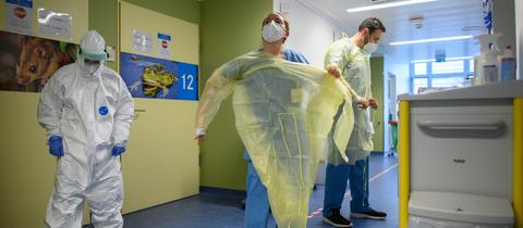 Mitarbeiter ziehen sich auf der Corona-Station in einer Klinik ihre Virenschutzkittel an.  (dpa)