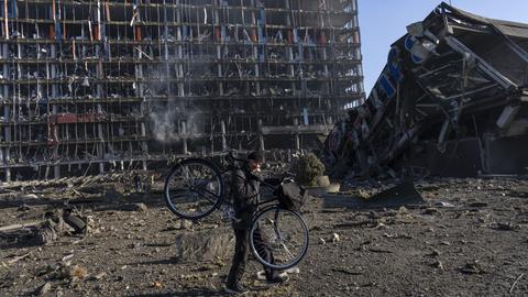Ein Mann trägt sein Fahrrad an einem durch Bombardierung zerstörten Einkaufszentrum in Kiew vorbei. (dpa)