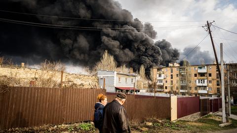 Zwei Personen gehen in Odessa (Ukraine) einen Weg entlang, während am Horizont schwarzer Rauch aufsteigt. (dpa)