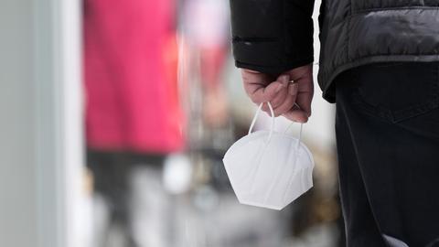 Ein Mann trägt auf der Dresdner Einkaufsstraße Prager Straße eine FFP-2-Maske in der Hand. (dpa)