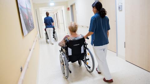 Zwei Pflegerinnen schieben Patienten mit Rollstühlen durch einen Flur. (dpa)