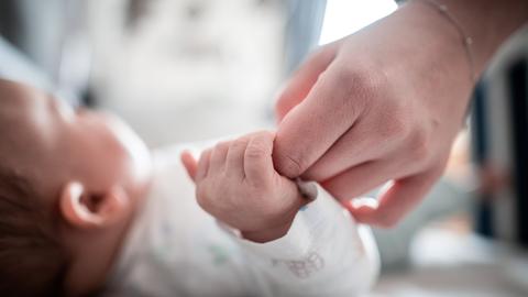 Ein Baby klammert sich an den Finger seiner Mutter.  (dpa)