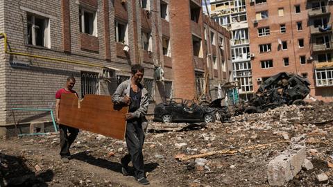 Zwei Menschen tragen eine Holzplatte durch einen zerbombten Wohnkomplex im Donbass. (dpa)