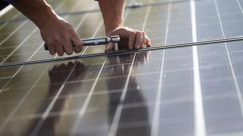 Hände montieren eine Photovoltaikanlage auf einem Dach (dpa)