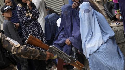 Ein Taliban-Kämpfer hält sein Gewehr in der Hand, während Menschen in Kabul auf die Verteilung von Lebensmitteln warten. (dpa)