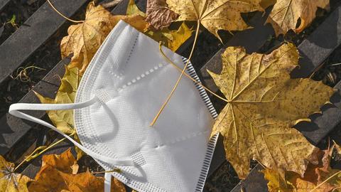 Eine Maske liegt auf einem Gehweg zwischen bunten Herbstblättern. (dpa)