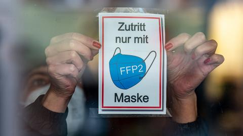 Hände kleben Schild mit dem Tragen einer FFP2-Maske als Zugangsvoraussetzung an eine Glastür (dpa)