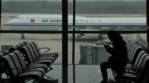 Eine Frau sitzt am Flughafen am Gate, im Hintergrund ist ein chinesisches Flugzeug zu sehen. (AP)