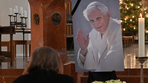 Eine Frau betet vor einem Bild des verstorbenen emeritierten Papst Benedikt XVI. in der Frauenkirche in München.  (dpa)