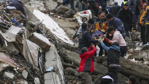  Menschen und Rettungskräfte bergen eine Person auf einer Bahre aus einem eingestürzten Gebäude in Adana (dpa)