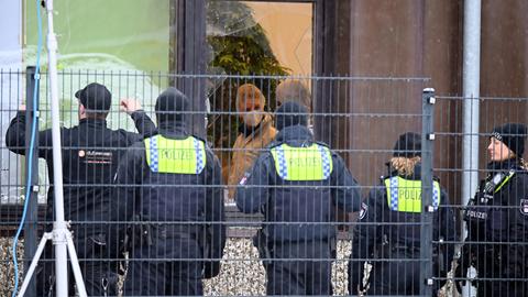 Polizisten sichern in Hamburg-Alsterdorf ein Gebäude, durch eine zerborstene Scheibe ist eine Beamtin in weißem Schutzanzug zu sehen. (dpa)