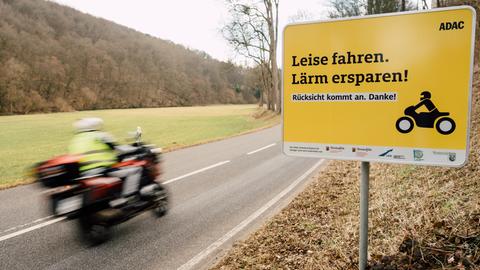 Ein Motorrad fährt an einem Schild mit der Aufschrift "Leise fahren. Lärm ersparen!" vorbei. ()