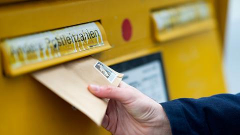 Hand wirft einen Brief in einen Briefkasten der Deutschen Post