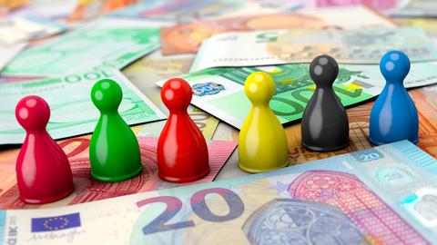 Spielfiguren in den Farben der Parteien, die im Bundestag vertreten sind, stehen auf Geldscheinen.