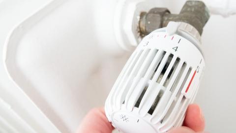 Hand dreht am Thermostat eines Heizkörpers