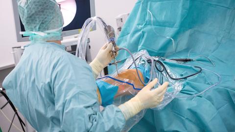 Ein Arzt steht in einem Operationssaal und operiert einen Patienten am Knie.