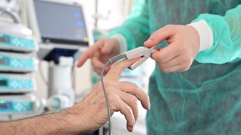 Ein Pfleger legt in einem Krankenzimmer im Klinikum Stuttgart bei einem Patienten ein Messgerät an.