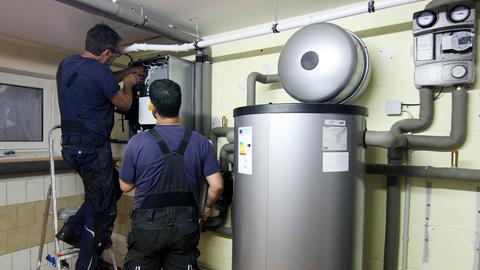 Zwei Handwerker stellen eine gerade installierte Wärmepumpe ein.