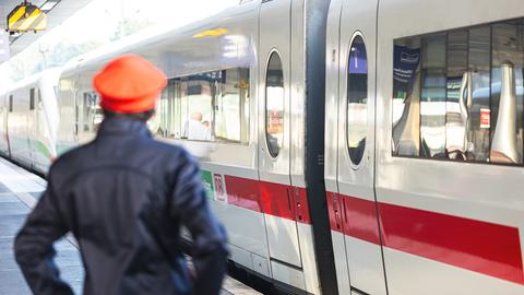 Ein Mitarbeiter der Deutschen Bahn (DB) steht neben einem ICE-Zug an einem Gleis im Bahnhof.