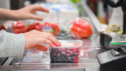 Eine Kassiererin scannt Heidelbeeren an der Kasse eines Supermarktes.
