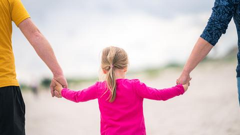 Ein Mädchen läuft Hand in Hand mit ihren Eltern am Strand entlang. (dpa)