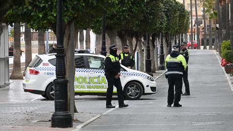 Polizisten stehen in Marbella neben einem Einsatzfahrzeug.