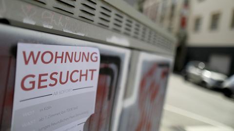 Mit einem Zettel an einer Hauswand suchen Menschen eine Wohnung.