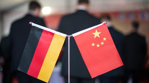 Flaggen der Bundesrepublik Deutschland und der Volksrepublik China stehen vor Menschen in Anzügen. (dpa)