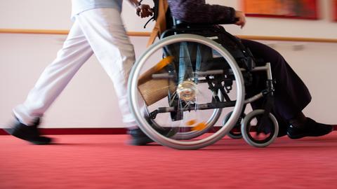 Ein Pfleger eines Pflegeheims schiebt eine Bewohnerin mit einem Rollstuhl.  (dpa)
