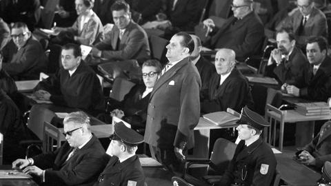 Am 20.12.1963 wird der erste Auschwitzprozess im Plenarsaal der Stadtverordnetenversammlung in Frankfurt am Main (Hessen) eröffnet. Das Bild zeigt die Reihe der Angeklagten mit ihren Verteidigern und den wachhabenden Polizisten. In der ersten Reihe sitzt der Angeklagte Victor Capesius (mit dunkler Brille), hinter ihm steht der Angeklagte Oswald Kaduk. 