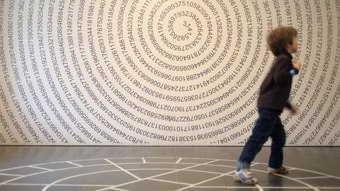 Ein Kind spielt im Mathematikum in Gießen vor einer Wand auf der die Zahl «Pi» dargestellt wird. 
