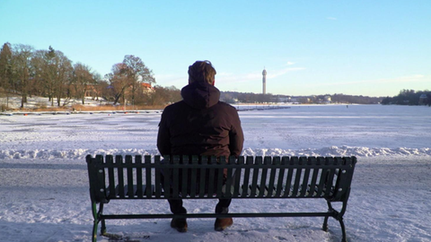 Mann sitzt auf Bank im Schnee