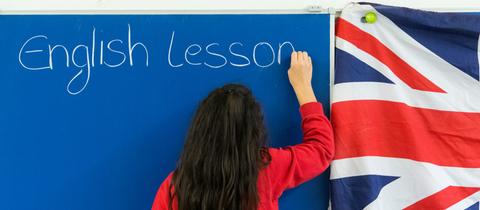 Schülerin schreibt "English lesson" an die Tafel. 