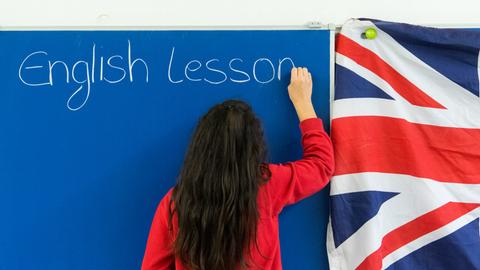 Schülerin schreibt "English lesson" an die Tafel. 