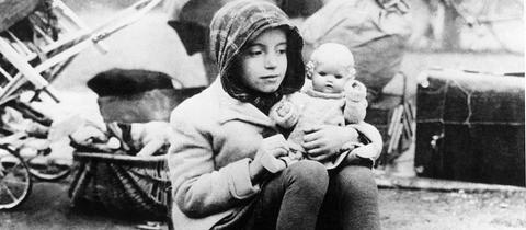 Ein Mädchen aus einem Flüchtlingstreck mit ihrer Puppe im Arm in den Wirren der Nachkriegszeit.