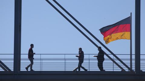 Menschen laufen über eine Brücke mit einer Deutschlandflagge. 
